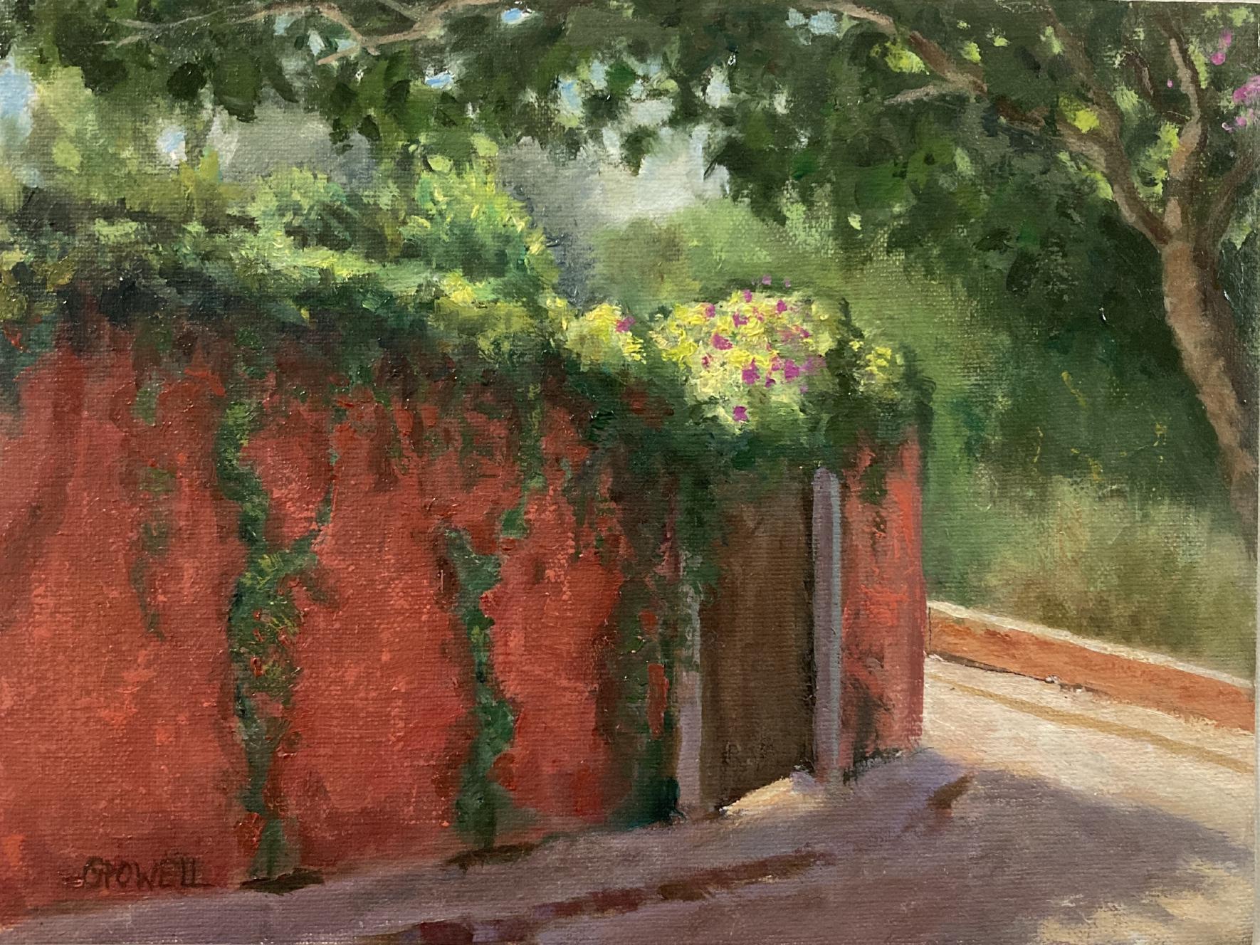 Bougainvillea climbs a red garden wall, in the shade of a tree and backlit by the sun.