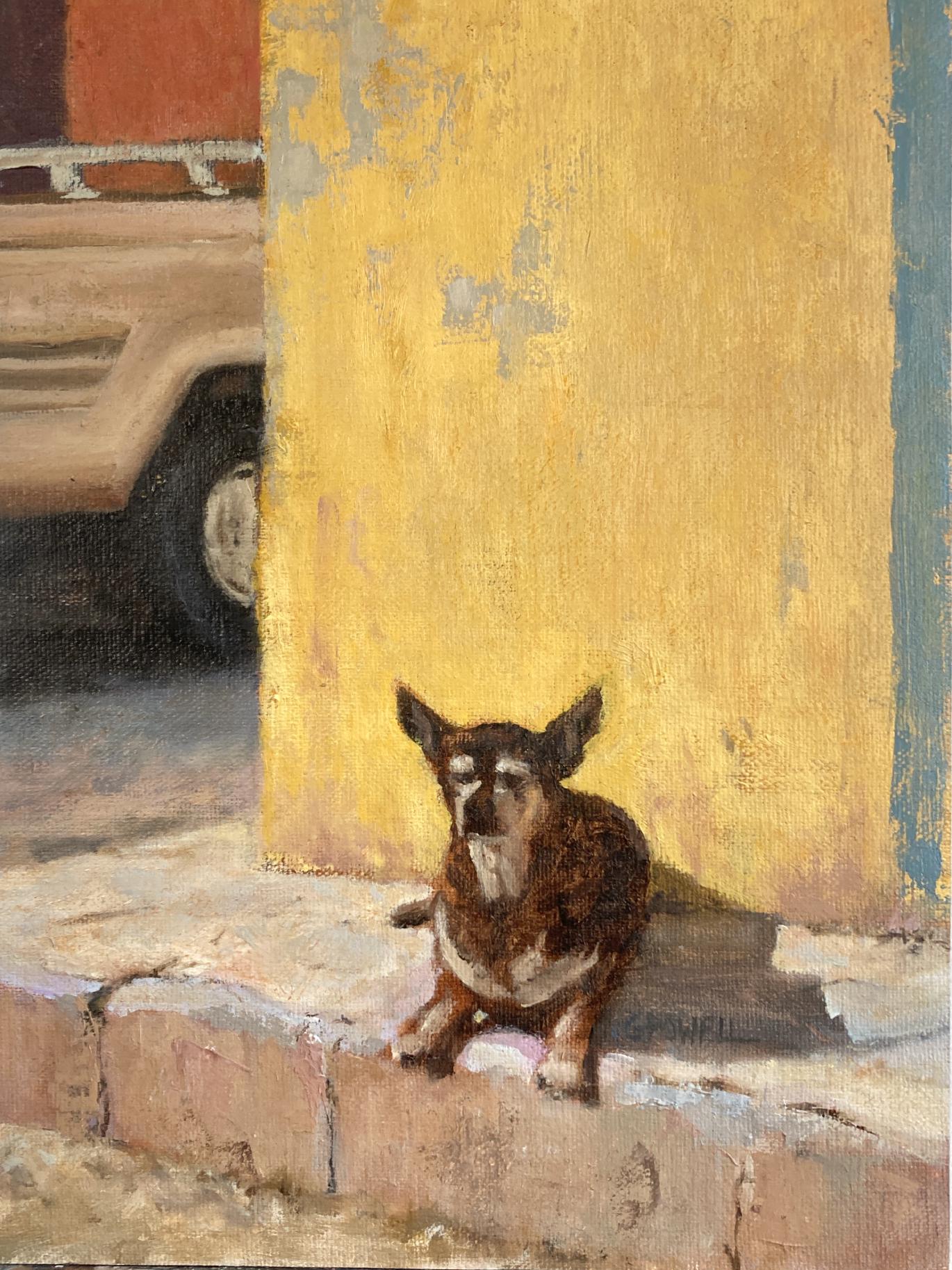 A small street dog lies on a curb against a yellow wall in Mexico. A pickup truck is passing by on the left.